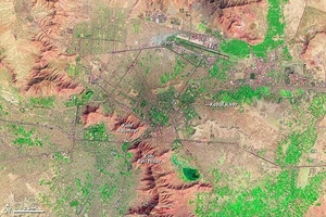 For more than 3,000 years, Kabul has occupied a strategic location along Central and Southern Asian trade routes. In the late eighteenth century, Kabul was established as Afghanistan's capital.
In this false-color satellite image vegetation appears fluorescent green, urban areas range in color from gray to black, and bare ground varies in color from beige to reddish brown. A mountain range, including Kohi Asamayi and Kohi Bini Hisar, snakes through the scene, running roughly northwest-southeast. More peaks appear in the northeast, right next to an airport. Urbanization appears densest at the city's center, just southwest of the airport, and it stretches out toward the right side of the image along an east-west highway. Leaping a mountain boundary, cityscape also fills the lower-left quadrant of the image.
Partly constrained by surrounding mountains, Kabul's primary direction for growth has been vertical, with multistory buildings constructed atop existing structures. Photo courtesy of NASA.