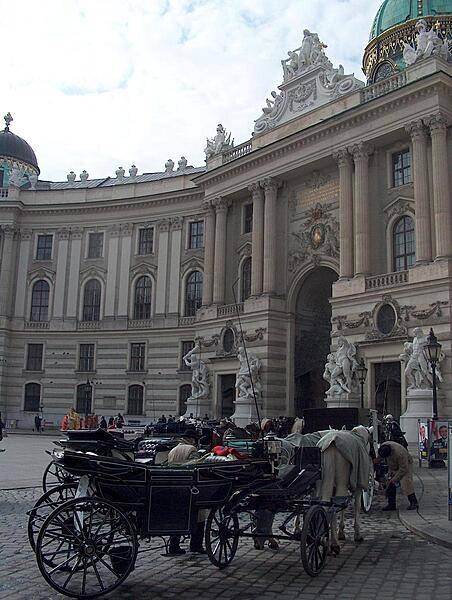 Horse-drawn coaches (known as fiaker in Vienna) await riders in front of the grand Michaelertrakt (Michael's Wing) of the Hofburg (Imperial Palace).