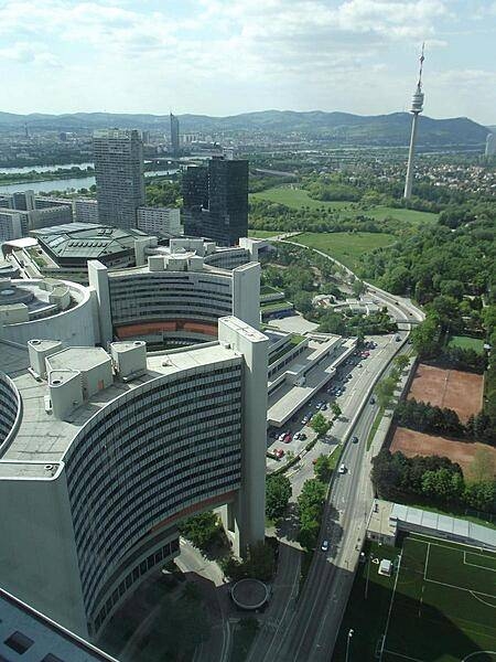 A bird's-eye view of two of the six Y-shaped office buildings, as well as the central cylindrical conference center, that make up part the United Nations Office complex in Vienna. In the distance is the 252 m (827 ft) Donauturn (Danube Tower) the tallest structure in Austria. In addition to its use as a communication tower, it also houses two revolving retaurants and has an observation deck.