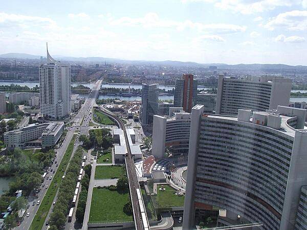 A view of the Kaisermuehlen section of Vienna looking across the Danube to the older, historic areas of the city. Part of the UN complex (also referred to as the Vienna International Center, VIC) appears on the right; the UN visitor center, entrance, and flag plaza are in the lower center. The subway line runs through the middle of the scene; the Kaisermuehlen-VIC metro station is at the center. The distinctive building on the left is the Hochhaus Neue Donau (High Rise New Danube), the tallest residential building in Austria.