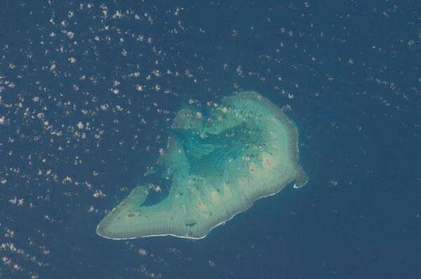 Ashmore Island (actually composed of three reef islets) is part of Ashmore Reef National Nature Reserve, which comprises several marine habitats, including seagrass meadows, intertidal sand flats, coral reef flats, and lagoons.
This astronaut photo from 2011 shows that the reef making up the island is not continuous but has several breaks that allow for current and sediment inflow.
A memorandum of understanding between the Australian and Indonesian Governments allows Indonesian fishermen access to their traditional fishing grounds within the region, subject to limits. Image courtesy of NASA.