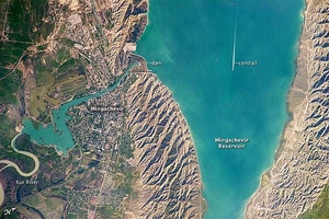 This astronaut photograph highlights the southern Mingachevir Reservoir in north-central Azerbaijan. The Mingachevir Reservoir occupies part of the Kura Basin, a topographic depression located between the Greater Caucasus Mountains to the northeast and the Lesser Caucasus Mountains to the southwest. The afternoon sun highlights distinctive parallel patterns in the hills that are the result of water and wind erosion of different rock layers exposed at the surface. The nearby city of Mingachevir (left) is split by the Kur River after it passes through the dam and hydroelectric power station complex at image top center. The current city was built in support of the hydroelectric power station constructed as part of the then-Soviet Union's energy infrastructure for the region. Today, Mingachevir is the fourth-largest city in Azerbaijan (by population), and it has become a cultural and economic center of the country. The width of the reservoir illustrated here is approximately 8 km (5 mi); a jet flying over the reservoir left a contrail midway between the shorelines. Photo courtesy of NASA.