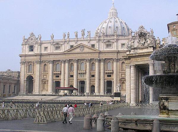 The facade of St. Peter's Basilica as viewed from next to one of the two matching Bernini fountains that grace St. Peter's Square (Piazza) in front of the church. The attic or upper story displays statues of Christ, his apostles, and St. John the Baptist. Constructed over a period of 80 years and consecrated in 1626, the basilica is the largest Christian church in the world - capable of holding some 60,000 people.