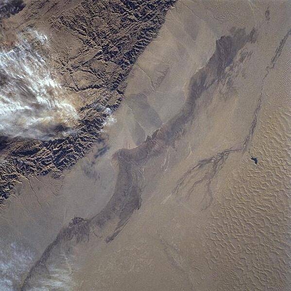 The rugged texture of the Altun Mountains (upper left) that forms part of the northern boundary of the Tibetan Plateau contrasts dramatically with the Takla Makan Desert of western China. Immediately north (to the right) of the mountains are large alluvial fans, gradually sloping downward in elevation. Sand dunes and sand ridges are visible along the northern (lower right) margin of the image. Click on photo for higher resolution. Image courtesy of NASA.