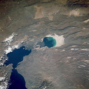 This near-vertical photograph shows Lac Assal (Lake Assal) in Djibouti, the third lowest surface in the world (excluding the ocean basins) and the lowest point in Africa at 155 m (510 ft) below sea level. Lake Assal sits in a rift valley, a depression where the earth's crust has split and adjacent areas have moved with respect to one another. The lake is located in the Danakil Desert near the western end of the Gulf of Aden. Because Lac Assal has no outlet, it is ten times saltier than the ocean and is the most saline body of water in the world. The evaporation rate of Lake Assal is very high because summer temperatures sometimes reach 52°C (125°F), and are accompanied by strong dry winds. The surrounding plain (visible on the image to the right of the lake), once the lake floor, is a glistening expanse of salt. The region surrounding the lake is mostly a stony desert with isolated plateaus and highlands. Lava flows from an ancient volcano are visible just to the left near the shore of the lake. Image courtesy of NASA.