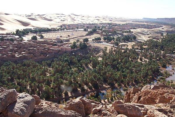 The oasis village of Taghit in the Sahara is known for its surrounding massive dunes. The oasis waters may be seen in the foreground. The site is southwest of Algiers, about 200 km (120 mi) from Beni Abbes.