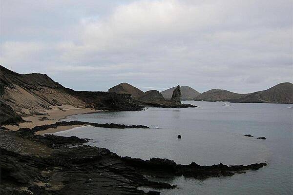 A beach on Bartholomew Island with a crater in the foreground and Pinnacle Rock in the background.