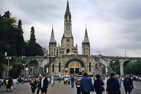 Pilgrims and visitors at Lourdes. The Rosary Basilica in the foreground serves as an entranceway to the larger Basilica of the Immaculate Conception behind. Lourdes is the reputed site of 18 Marian apparitions in 1858. The town is one of the world's greatest pilgrimage sites hosting some 5 million visitors annually.