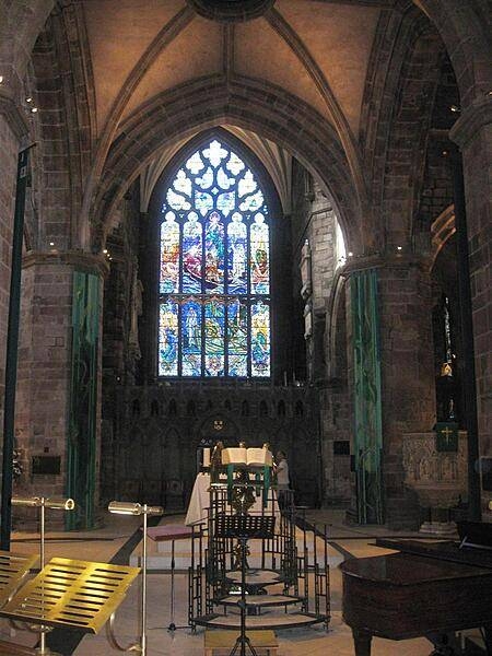 A view of the North Transept inside Edinburgh's Saint Giles Cathedral and the great North Window completed by Douglas Strachan, Scotland's most prolific stained glass artist of the 20th century. This window portrays nautical themes: Christ walking on water in the lower section and, in the upper section, Christ calming a tempest; it is one of the most dynamic artworks in the church exhibiting swirling shapes in the glass pieces, and a predominance of blues, greens, and purples in the color composition.