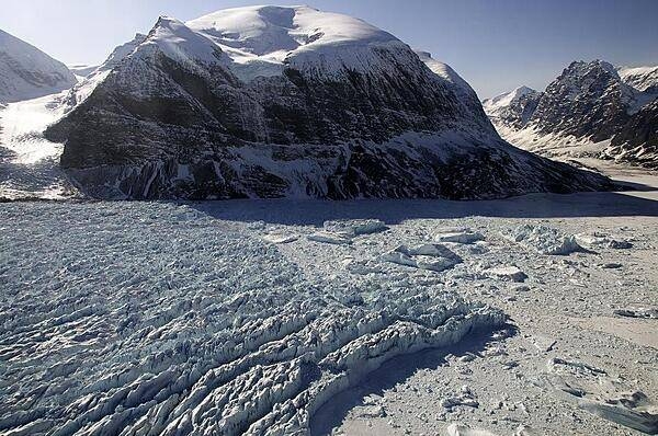 The calving front of Kangerdlugssup Glacier in central west Greenland where icebergs are born. You can see several large ice bergs in the fjord on the right surrounded by the so called mélange, which is a dense mix of bergy bits and sea ice floating in the fjord. The mélange plays a role in how many ice bergs a glacier can produce by stabilizing the calving front. Credit: NASA/Michael Studinger.