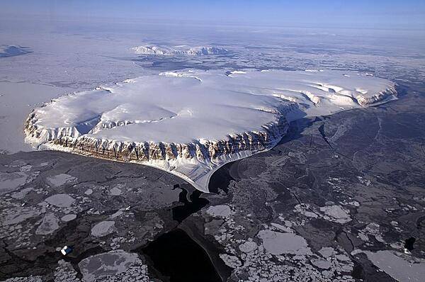 This image of Saunders Island and Wolstenholme Fjord with Kap Atholl in the background was taken during a NASA Operation IceBridge survey flight in April of 2013. Sea ice coverage in the fjord ranges from thicker, white ice seen in the background, to thinner grease ice and leads showing open ocean water in the foreground. Credit: NASA/Michael Studinger.