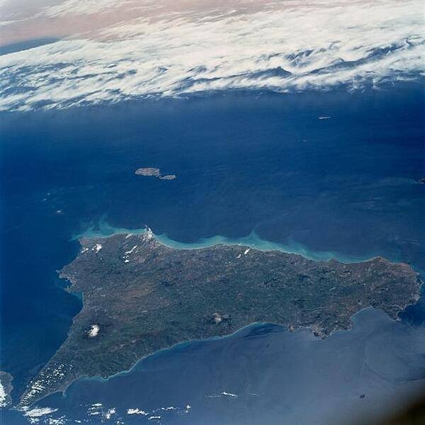 This southerly-looking view taken from onboard the space shuttle, shows the triangular-shaped island of Sicily. With only very limited coastal plains, the island's topography consists of rugged hills and low mountains. Snow-capped Mt. Etna is visible near the northeast point of the island. Some other distinctive features in this image are the lighter-colored zone of suspended sediment in the water along the southern coast, in the middle distance, the smaller islands of Malta, and off to the south, across the Mediterranean, the north African shore. Image courtesy of NASA.