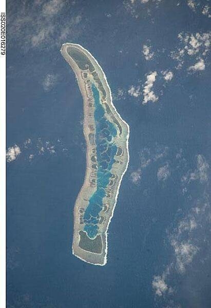 Millennium Island - known as Caroline Island prior to 2000 - is located at the southern end of the Line Islands, which make up the western portion of Kiribati. Uninhabited Millennium Island is formed from a number of smaller islets built on coral reefs. The reefs grew around a now-submerged volcanic peak, leaving a ring of coral around an inner lagoon. The shallow lagoon waters are a lighter blue than the deeper surrounding ocean water; tan linear "fingers" within the lagoon are the tops of corals. The two largest islets are Nake Islet (on the north) and South Islet. Image courtesy of NASA.