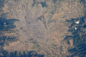 The capital and largest city of Nepal, Kathmandu, occupies much of the valley located near the center of the country. Nepal is home to much of the Himalaya mountain range between Tibet (China) to the north and India to the south. Geological and fossil evidence indicates that the Kathmandu Valley was covered by a large lake between approximately 2.8 million and 10,000 years ago. Paleo-Kathmandu Lake is thought to have drained in phases due to the drying of the regional climate; continuing mountain building-tectonic uplift and faulting-in the region; and the formation of an integrated drainage system, as river channels cut through previous rock ridge dams.
The green, vegetated slopes that ring the Kathmandu metro area (light gray, image center) include both forest reserves and national parks. The metropolitan area is relatively flat compared to the surrounding mountains. Tribhuvan International Airport, near the eastern margin of the city, is the only international airport in Nepal. 
Archeological evidence suggests that the human development of Kathmandu, together with the nearby "sister cities" of Lalitpur and Bhaktapur, began almost 2,000 years ago. Today, the three cities form the governmental, cultural, and-as a main access point to the Himalayas for tourism-economic center of the country. Photo courtesy of NASA.