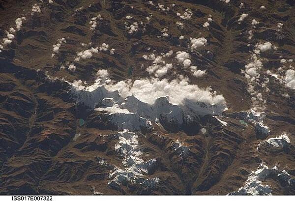 This view of the Peruvian Andes was taken looking east from the international space station flying off the Peruvian coast and shows Cordillera Huayhuash (pronounced Why-wash). Here clouds are banked up on the east side, snow covers all higher slopes and mountain peaks, and glaciers occupy lower slopes. This prominent but short mountain range (25 km or 15 mi in length) boasts twenty peaks of remarkable steepness and ridge sharpness. Although only 100 km (60 mi) from the coastline, six of the peaks reach above 6,000 m (more than 19,500 ft), the highest of which is Nevado Yerupaja, Peru's second highest peak, variously estimated as 6,617 and 6,635 m high. Generally considered the most spectacular peak in South America, Yerupaja is so steep that it has seldom been climbed. Photo courtesy of NASA.