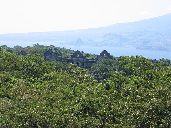 A view of Topside - the highest area of Corregidor - taken from the vicinity of the Spanish Lighthouse. Shown are the remains of the "Mile-Long Barracks" barely visible above the trees. These main barracks on the Topside section housed the troops of the coast artillery battalions who manned the island defenses. The building was a three-story concrete structure designed to be hurricane proof while providing comfortable, airy accommodations in a tropical environment. Despite the fact it never was a mile long when built, the structure was considered the longest barracks in the world. In the background, across the North Channel, are the mountains of Bataan Peninsula overlooking Corregidor.
