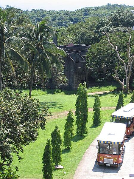 Tour busses pause in the vicinity of the Spanish Lighthouse on the island of Corregidor. In the background, amid the trees, are the remains of one of the senior officer's family quarters.