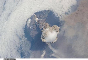 A fortuitous orbit of the International Space Station allowed the astronauts to take this striking view of Sarychev Peak volcano (Russia's Kuril Islands, northeast of Japan) in an early stage of eruption on 12 June 2009. Sarychev Peak is one of the most active volcanoes in the Kuril Island chain and is located on the northwestern end of Matua Island. Prior to 12 June, the last explosive eruption had occurred in 1989 with eruptions in 1986, 1976, 1954, and 1946 also producing lava flows.
This detailed photograph is exciting to volcanologists because it captures several phenomena that occur during the earliest stages of an explosive volcanic eruption. The main column is one of a series of plumes that rose above Matua Island on June 12. The plume appears to be a combination of brown ash and white steam. The vigorously rising plume gives the steam a bubble-like appearance; the surrounding atmosphere has been shoved up by the shock wave of the eruption. The smooth white cloud on top may be water condensation that resulted from rapid rising and cooling of the air mass above the ash column, and is probably a transient feature (the eruption plume is starting to punch through).
The structure also indicates that little or no shearing winds were present at the time to disrupt the plume. By contrast, a cloud of denser, gray ash - most probably a pyroclastic flow - appears to be hugging the ground, descending from the volcano summit. The rising eruption plume casts a shadow to the northwest of the island (bottom center).
Brown ash at a lower altitude of the atmosphere spreads out above the ground at upper right. Low-level stratus clouds approach Matua Island from the east, wrapping around the lower slopes of the volcano. Only about 1.5 km (1 mi) of the coastline of Matua Island (upper center) can be seen beneath the clouds and ash. Image courtesy of NASA.
