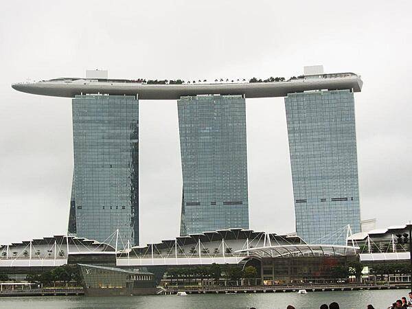 View of the Marina Bay Sands complex in Singapore that opened in 2010 and has since become a city landmark. The three 55-story towers contain hotel rooms. The upper level Sky Park, built to resemble a ship, has the world's longest elevated swimming pool, restaurants, gardens, and a public observation deck. The integrated resort also includes an adjacent ArtScience Museum, a casino, and a convention center.