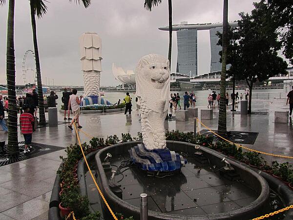 Smaller of the two Merlions (lion head and body of a fish) along the Singapore River. The word "Sing" comes from the Malay word for lion; thus the city is often called "Lion City." In the background looms the back of the statue of the larger Merlion, the Marina Bay Sands Hotel built to resemble a ship on towers, and the lotus flower-shaped ArtScience Museum.