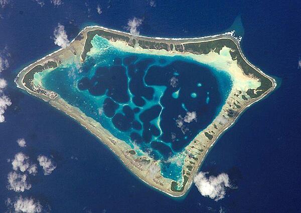 At roughly 8 km (5 mi) wide, Atafu Atoll is the smallest of three atolls comprising Tokelau. Land area is only about 2.5 sq km and the lagoon's area is about 15 sq km. The primary settlement on Atafu is a village located at the northwestern corner of the atoll - indicated by an area of light gray dots in the left part of this photograph. The typical ring shape of the atoll is the result of coral reefs building up around a former volcanic island. Over geologic time, the central volcano subsided beneath the water surface, leaving the fringing reefs and a central lagoon that contains submerged coral reefs. Image courtesy of NASA.