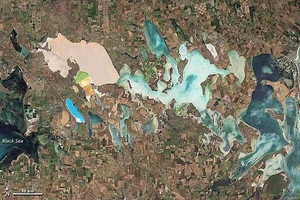 From mainland Ukraine, the Crimean Peninsula extends southward, bordered on the west by the Black Sea and on the east by the Sea of Azov. Stretching across the peninsula is a network of shallow, marshy inlets sprawling over roughly 2,600 sq km (1,000 sq mi). This network of lagoons is known as Syvash (also Sivash or Sivas). During the summer months, the warmed marsh waters give off unpleasant odors, lending the region the nicknames of "Rotten Sea" or "Putrid Sea."
This natural-color satellite image shows the shallow waters and varied chemical composition of the Syvash lagoons contribute to their unearthly colors of peach, mustard, lime green, blue, blue-green, beige, and brown. Thick layers of silt coat the bottoms of the shallow marshes, which are rich enough in mineral salts to supply a local chemical plant.
Surrounding the marshy areas are mostly agricultural fields. Urbanized areas appear along the shores of the Black Sea, and highways curve and zigzag across the peninsula. Outside of the marshes, the land in this area is generally a level plain of arid steppe. In colder months, frosts alternate with thaws, and fogs are frequent. Photo courtesy of NASA.