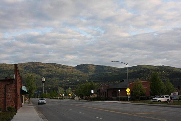 A typical wide road in Post Falls, Idaho, with a mountain view and a western-style building on one side, and a contemporary building on the other.
