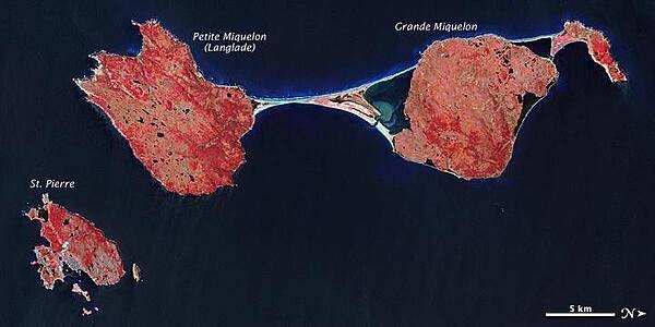 The last remnant of France's once-vast holdings in North America, this island archipelago off the coast of Newfoundland bears the scars of a complicated geologic history. Saint Pierre and Miquelon cover just 242 sq km (93 sq mi), and the three biggest islands lend the entire archipelago its name.
In this false-color satellite image, vegetation appears in varying shades of pink and red, bare land is beige, urbanized areas are blue-gray, and water appears in shades of blue and blue-green.
Saint Pierre is the smallest of the archipelago's major islands, a mostly northeast-southwest running landmass with several smaller islands and islets scattered around it. In the west (top of the image), Miquelon consists of three main sections: an arc-shaped body in the north (top right), Grande Miquelon immediately southeast of that, and Langlade (or Petite Miquelon) Island in the south. Grande Miquelon and Langlade are connected by a tombolo, a ridge of beach material (typically sand), built by wave action, that connects an island to the mainland. This tombolo formed in the eighteenth century.
The terrain of the archipelago consists of mostly barren rock. Deforestation has claimed much of the vegetation, although woodland still covers 20 percent of the surface. Scrub vegetation and peatland are extensive. Cold, wet, foggy weather predominates, with windy springs and autumns. 
The islands, particularly Langlade, bear a scoured appearance, and this is no coincidence. During the Pleistocene Ice Age, glacial ice scraped the island. Today, wind and waves continue to erode these landmasses. For several months a year, winds regularly exceed 60 km (35 mi) per hour, and frequent storms pound the coastlines with high waves. Anecdotal evidence from local fishermen suggests that recent mild winters and less extensive sea ice might have allowed more erosion by ocean waves. Photo courtesy of NASA.