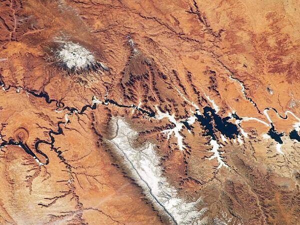 The Colorado Plateau spans northern Arizona, southern Utah, northwestern New Mexico, and southwestern Colorado and is well known for its striking landscapes and broad vistas - an impression enhanced in this view from the International Space Station. This astronaut photograph highlights part of the Utah-Arizona border region of the Plateau, and includes several prominent landforms. The Colorado River, dammed to form Lake Powell in 1963, crosses from east to west (which is left to right here because the astronaut was looking south; north is towards the bottom of the image). The confluence of the Colorado and San Juan Rivers is also visible. Sunglint - sunlight reflected off a water surface back towards the observer - provides a silvery, mirror-like sheen to some areas of the water surfaces. The geologic uplift of the Colorado Plateau led to rapid downcutting of rivers into the flat sedimentary bedrock, leaving spectacular erosional landforms. One such feature, The Rincon (left center), preserves evidence of a former meander bend of the Colorado River. Photo courtesy of NASA.