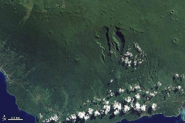 At the western end of the Samoan Island chain lies Savai'i. Stretching over 1,682 sq km (649 sq mi), Savai'i is one of the largest landmasses in Polynesia. The mountainous island is a shield volcano that reaches its highest altitude, 1,858 m (6,095 ft), near the center of the island. The region's tropical, humid climate sustains vegetation that carpets much of the island.
A jagged line of small, round volcanic craters extends east-west across the island (top of image). South of this uneven line, two deep, parallel valleys extend toward the south. The semicircular contours of the valleys suggest that they might be the remains of an ancient caldera or collapsed magma chamber that was modified by the later eruption of additional lava.
With the exception of a few brown crater rims, and a coastal settlement along the image's left edge, the landscape appears in varying shades of green. Dense rainforests cover the island's rugged interior, and thick vegetation also thrives along the coastal plains. 
Savai'i has remained volcanically active into historical times, with two eruptions occurring in the early 20th century. The eruptions sent big lava flows to the island's northern coast, destroying several villages. Photo courtesy of NASA.